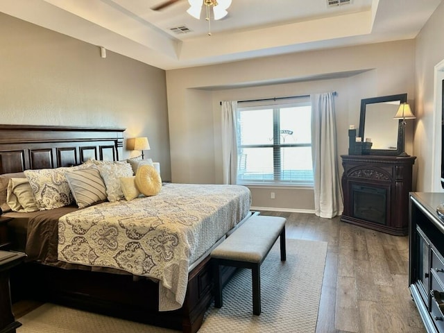 bedroom featuring a raised ceiling, visible vents, and wood finished floors