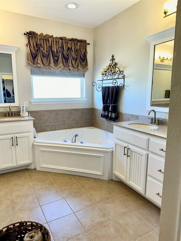 full bath featuring two vanities, a sink, a garden tub, and tile patterned floors