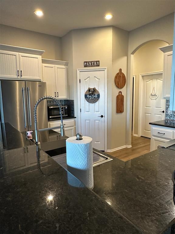 kitchen with arched walkways, dark stone counters, white cabinets, high quality fridge, and recessed lighting