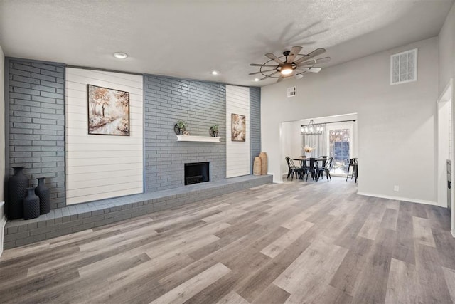 unfurnished living room with a fireplace, light hardwood / wood-style flooring, a textured ceiling, and ceiling fan