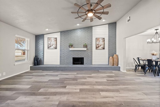 living room featuring vaulted ceiling, light hardwood / wood-style flooring, a textured ceiling, a fireplace, and ceiling fan with notable chandelier