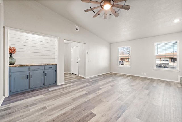 unfurnished living room with ceiling fan, lofted ceiling, light hardwood / wood-style floors, and a textured ceiling