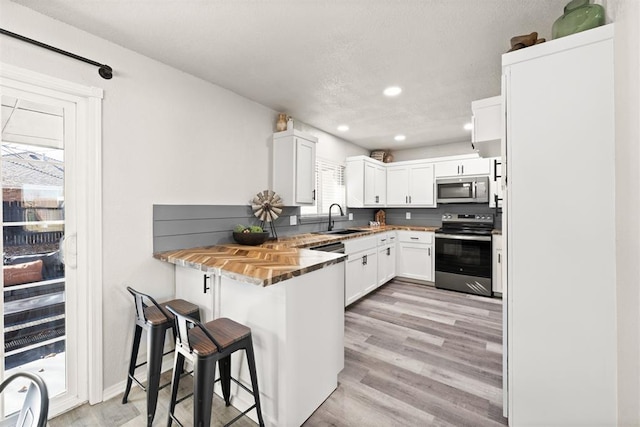 kitchen featuring sink, a breakfast bar area, white cabinetry, stainless steel appliances, and kitchen peninsula