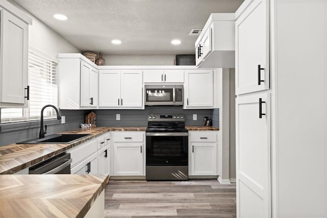 kitchen with appliances with stainless steel finishes, white cabinetry, sink, a textured ceiling, and light hardwood / wood-style flooring