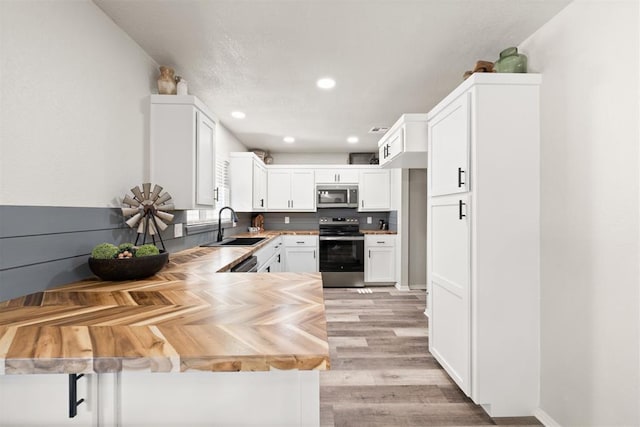 kitchen with sink, wooden counters, white cabinetry, stainless steel appliances, and kitchen peninsula