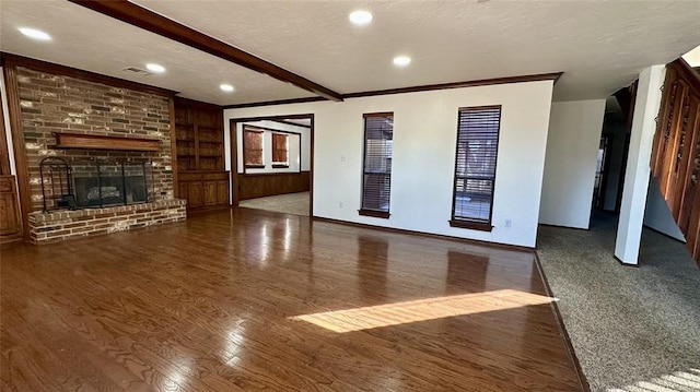 unfurnished living room with beamed ceiling, a brick fireplace, dark wood-type flooring, and a textured ceiling