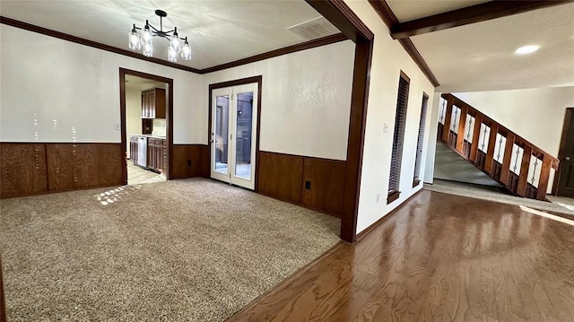 spare room featuring french doors, ornamental molding, light colored carpet, and wood walls