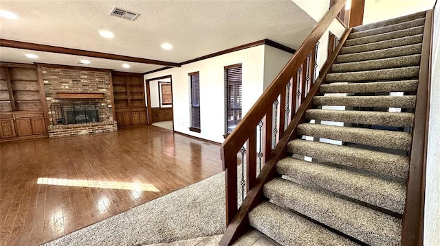 stairway with beam ceiling, a textured ceiling, ornamental molding, hardwood / wood-style flooring, and a fireplace