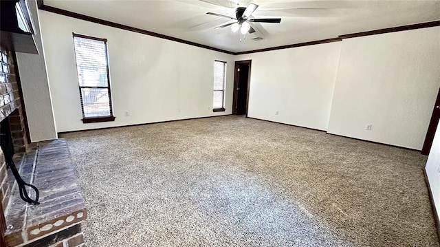 empty room featuring a brick fireplace, crown molding, ceiling fan, and carpet