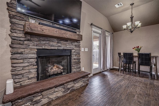 living room featuring dark wood-type flooring, an inviting chandelier, a stone fireplace, and vaulted ceiling