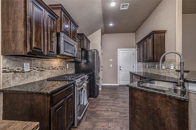 kitchen featuring sink, dark stone countertops, stainless steel appliances, dark hardwood / wood-style floors, and dark brown cabinetry