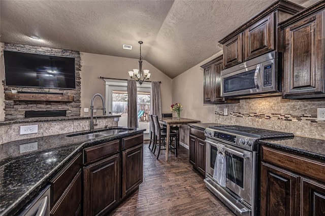 kitchen with sink, stainless steel appliances, dark brown cabinetry, decorative light fixtures, and vaulted ceiling