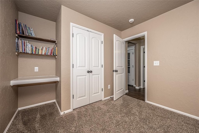 unfurnished bedroom with a closet, a textured ceiling, and dark colored carpet