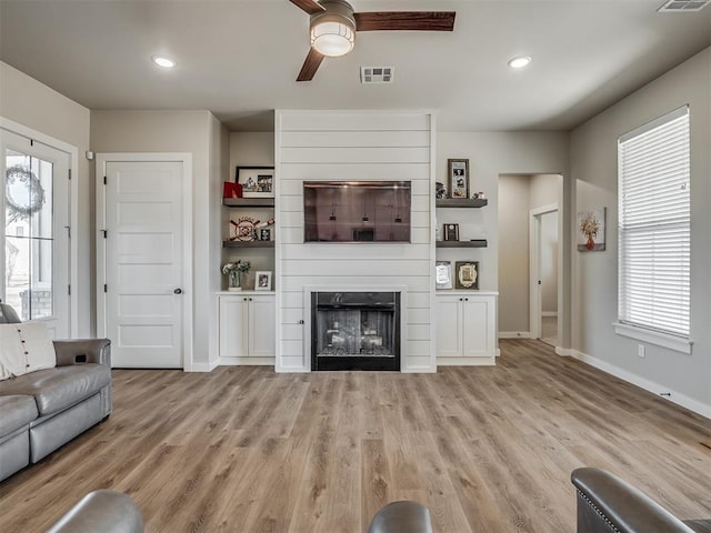 unfurnished living room with ceiling fan, a large fireplace, and light wood-type flooring