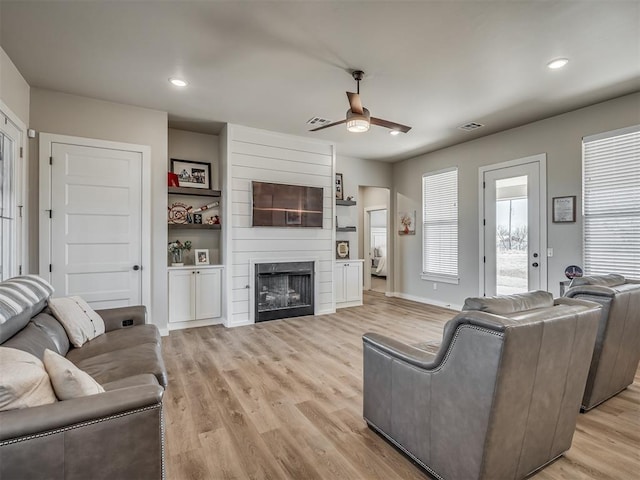 living area featuring baseboards, recessed lighting, ceiling fan, light wood-type flooring, and a large fireplace