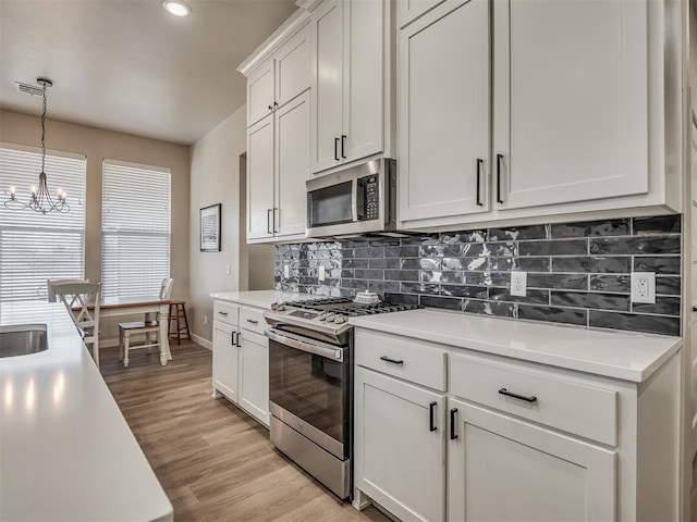 kitchen featuring appliances with stainless steel finishes, white cabinetry, backsplash, hanging light fixtures, and light wood-type flooring