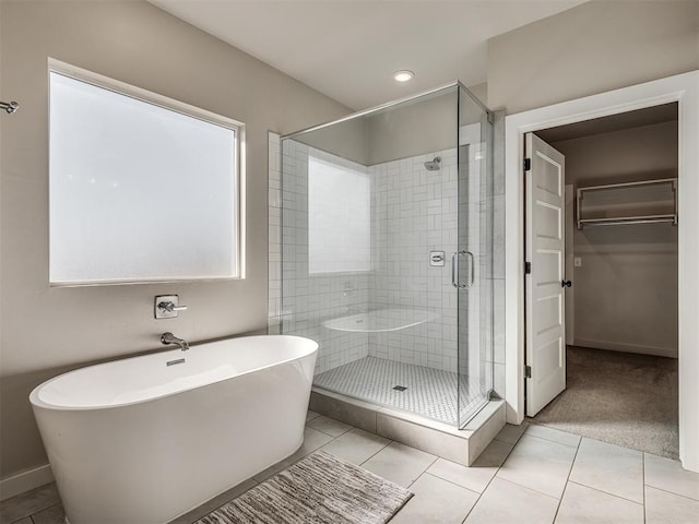 bathroom with baseboards, a soaking tub, a stall shower, a walk in closet, and tile patterned floors