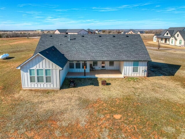 back of property with a patio area, a lawn, board and batten siding, and a shingled roof