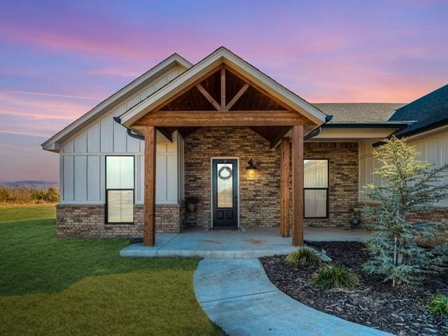 exterior entry at dusk with brick siding, a lawn, and board and batten siding