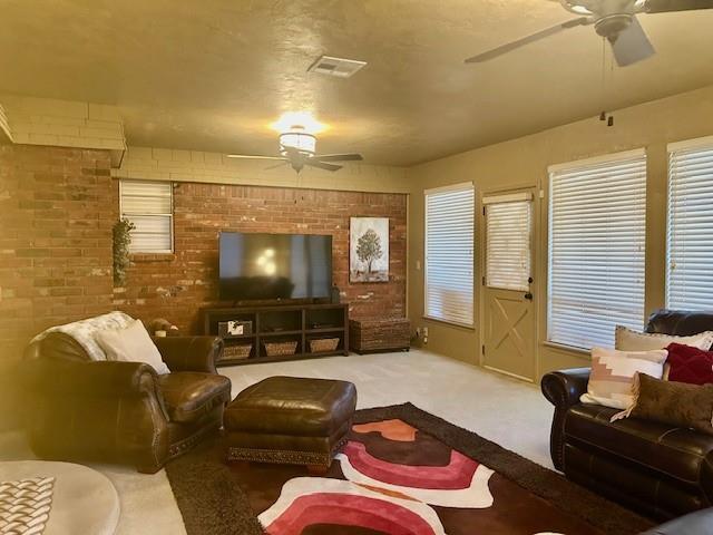 carpeted living room with brick wall and ceiling fan