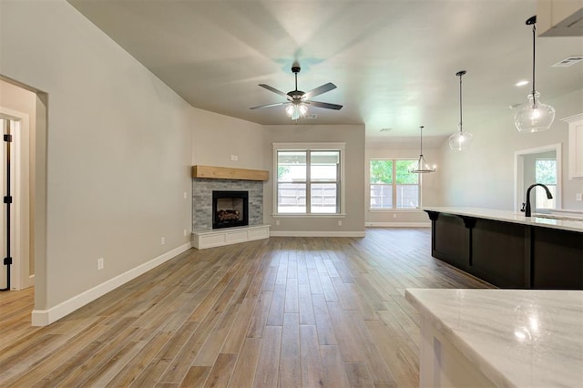 unfurnished living room featuring ceiling fan, a stone fireplace, sink, and light hardwood / wood-style floors