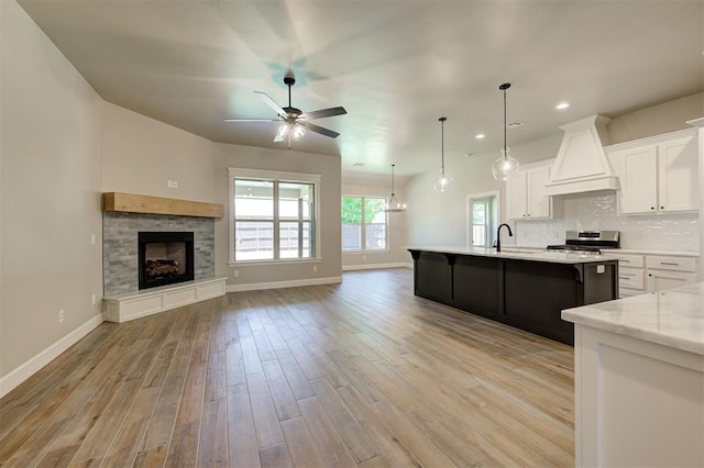 kitchen with stainless steel electric range, white cabinetry, a center island with sink, decorative light fixtures, and custom exhaust hood