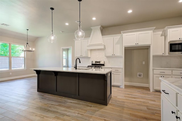 kitchen with white cabinetry, stainless steel appliances, decorative light fixtures, and an island with sink