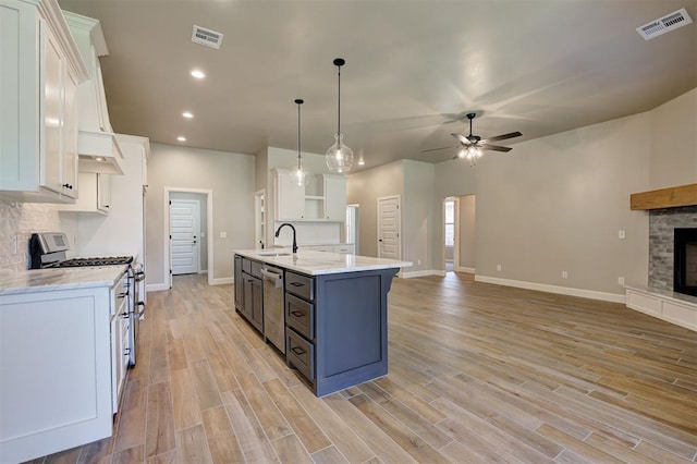 kitchen featuring sink, stainless steel appliances, an island with sink, white cabinets, and decorative light fixtures