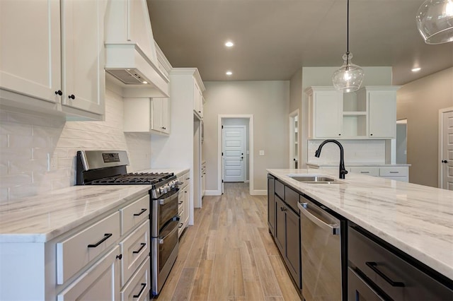 kitchen featuring pendant lighting, sink, premium range hood, white cabinetry, and stainless steel appliances