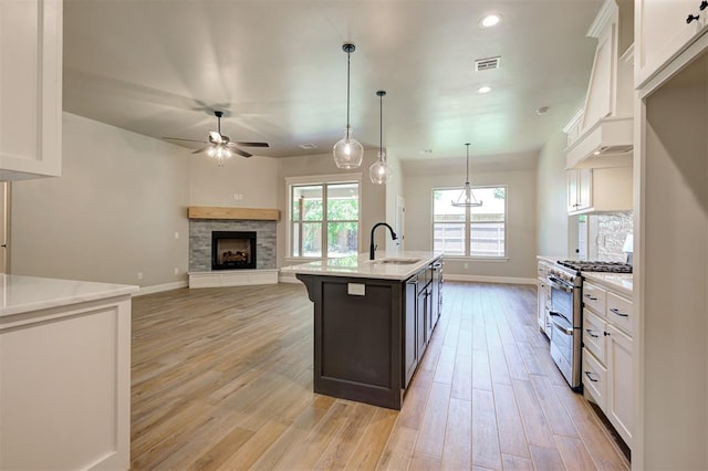 kitchen featuring white cabinetry, sink, hanging light fixtures, double oven range, and a center island with sink