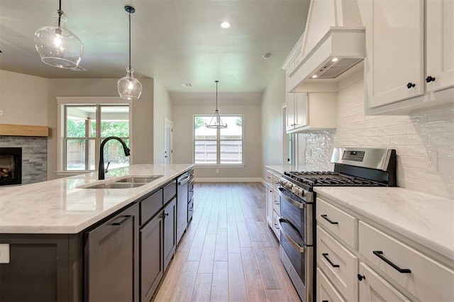 kitchen with white cabinetry, stainless steel appliances, light stone counters, custom range hood, and an island with sink