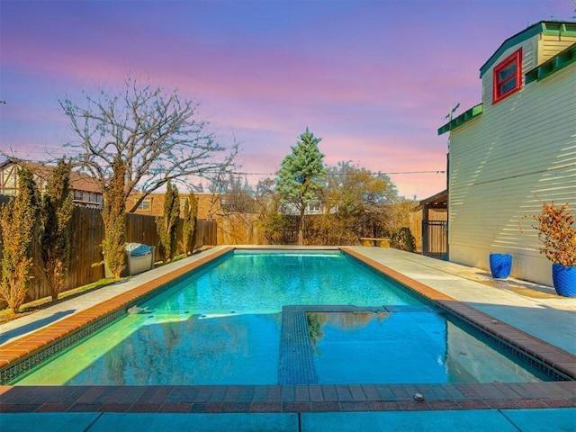 pool at dusk with a fenced backyard and a pool with connected hot tub