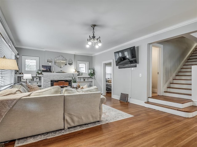 living area with a warm lit fireplace, a chandelier, wood finished floors, ornamental molding, and stairway