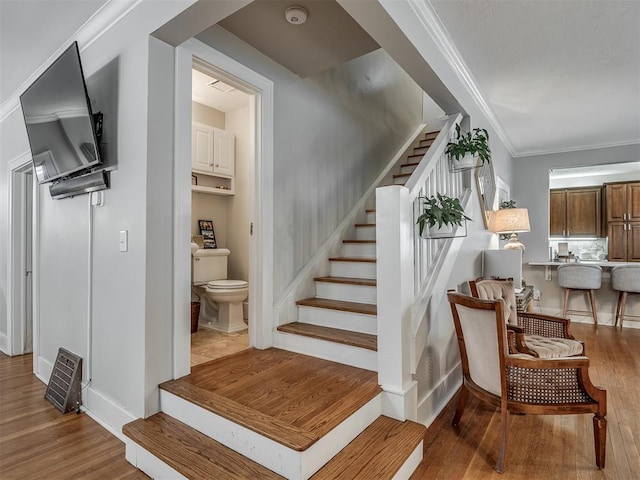 stairway with ornamental molding, wood finished floors, and baseboards