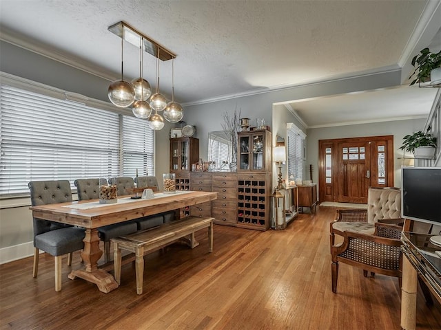 dining space featuring light wood finished floors, baseboards, ornamental molding, and a textured ceiling