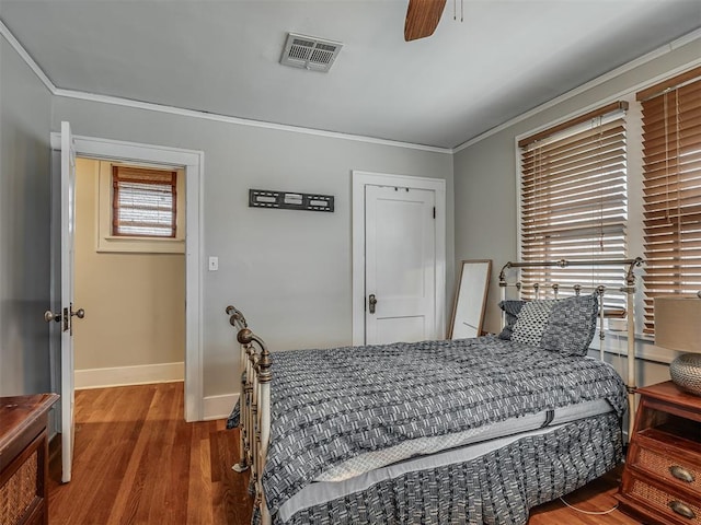 bedroom with baseboards, visible vents, a ceiling fan, ornamental molding, and wood finished floors