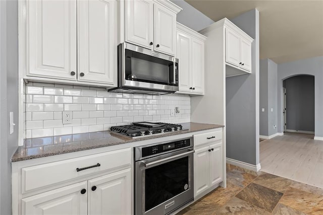 kitchen featuring stainless steel appliances, white cabinetry, dark stone countertops, and backsplash