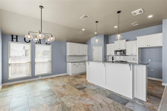 kitchen featuring hanging light fixtures, white cabinetry, a center island with sink, and backsplash