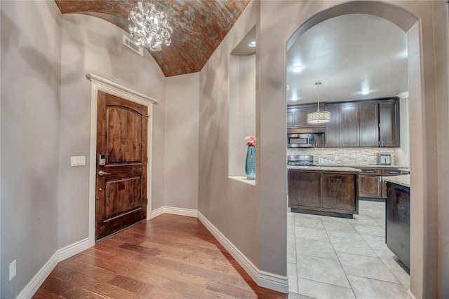 foyer featuring lofted ceiling, brick ceiling, light hardwood / wood-style floors, and a chandelier