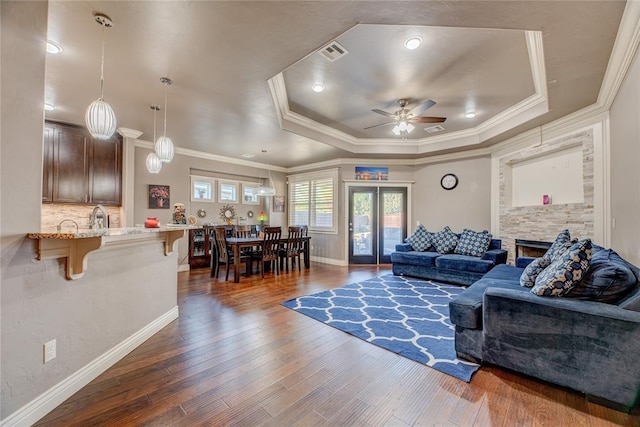 living room with dark wood-type flooring, a fireplace, a tray ceiling, and crown molding