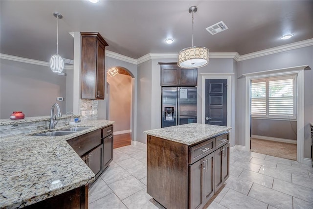 kitchen with sink, hanging light fixtures, a center island, light stone counters, and stainless steel refrigerator with ice dispenser