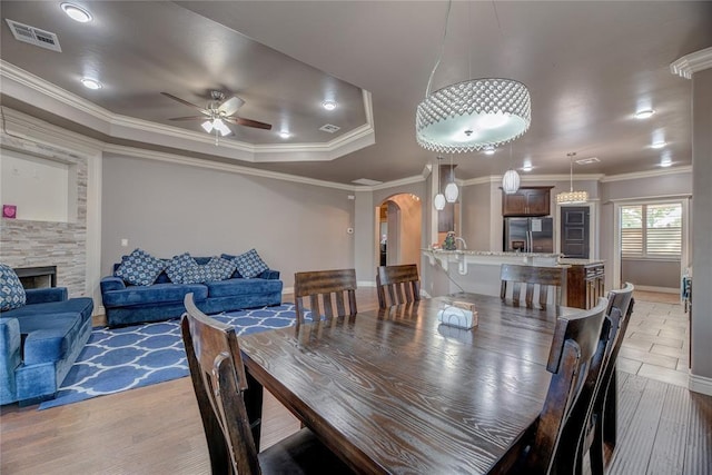 dining space with crown molding, a stone fireplace, ceiling fan, and hardwood / wood-style flooring