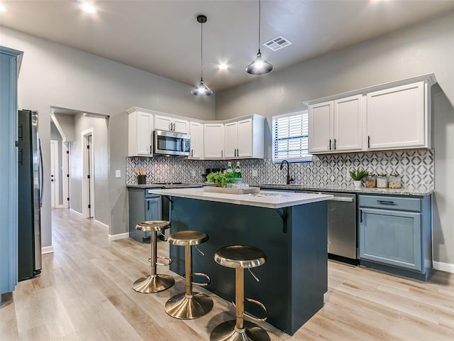 kitchen with decorative light fixtures, a center island, appliances with stainless steel finishes, a kitchen breakfast bar, and white cabinets