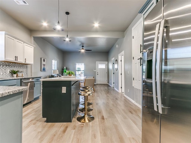 kitchen featuring decorative light fixtures, appliances with stainless steel finishes, a kitchen breakfast bar, a kitchen island, and white cabinets