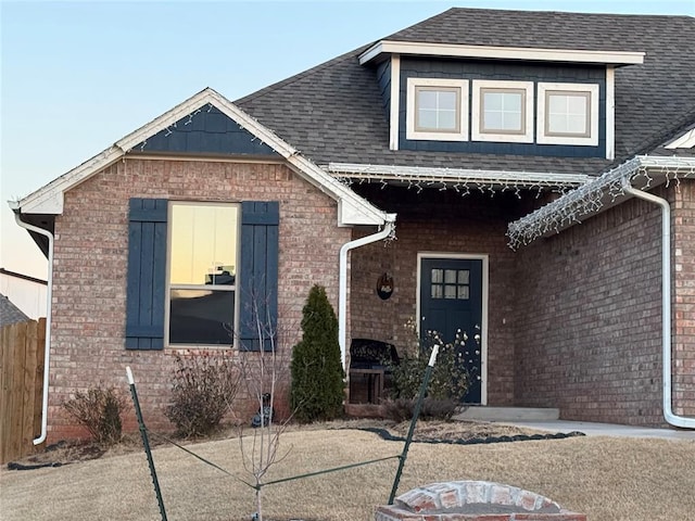 view of front of property featuring a shingled roof, fence, and brick siding