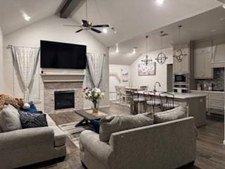 living area featuring high vaulted ceiling, beamed ceiling, a fireplace, and wood finished floors