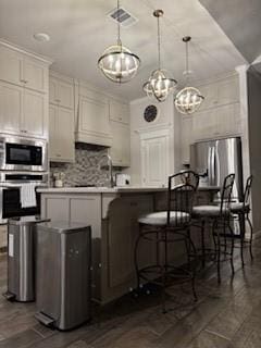 kitchen featuring white cabinetry, appliances with stainless steel finishes, decorative light fixtures, and a breakfast bar area