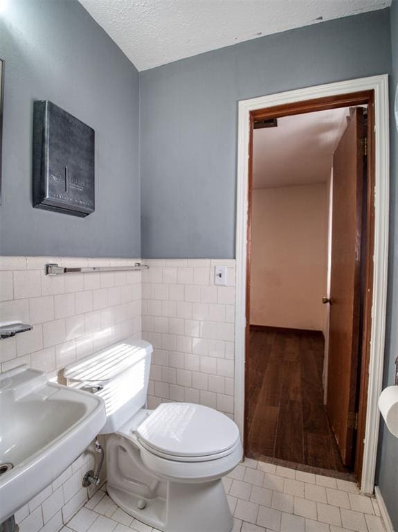 bathroom featuring toilet, sink, tile walls, a textured ceiling, and tile patterned flooring