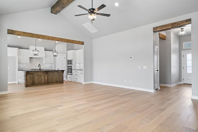 unfurnished living room featuring ceiling fan, high vaulted ceiling, light wood-style flooring, a sink, and beamed ceiling