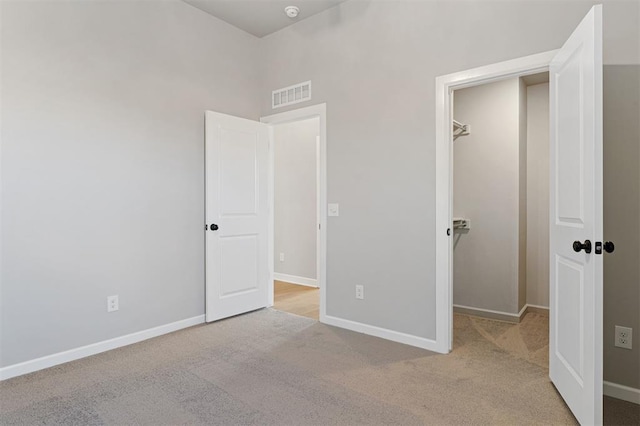 unfurnished bedroom featuring a walk in closet, visible vents, light carpet, and baseboards